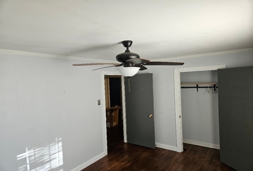 Unfurnished bedroom with a barn door, crown molding, dark wood-type flooring, a closet, and a ceiling fan