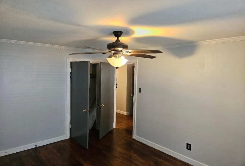 Unfurnished bedroom with ornamental molding, dark wood finished floors, a ceiling fan, and a closet