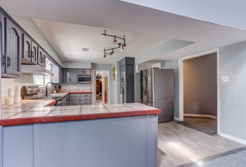 Kitchen with tile counters, stainless steel appliances, light wood-type flooring, a peninsula, and under cabinet range hood