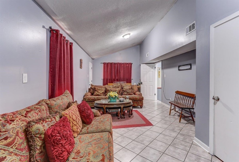 Living room with light tile patterned floors, a textured ceiling, and vaulted ceiling