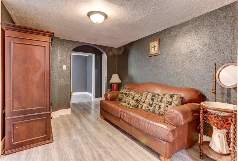 Living area featuring arched walkways, a textured wall, light wood finished floors, and a textured ceiling