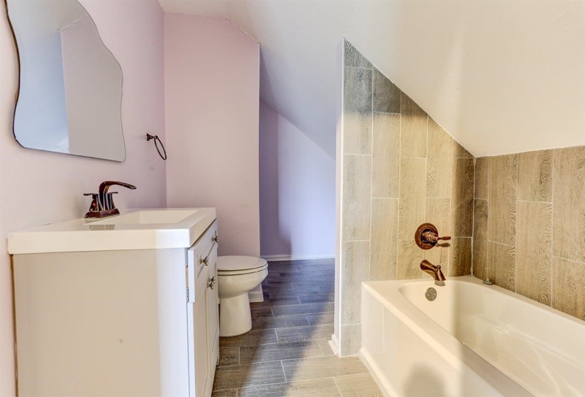 Full bath featuring a garden tub, vanity, lofted ceiling, and wood finish floors