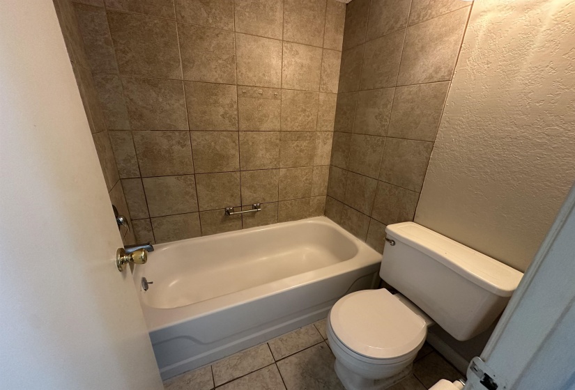 Bathroom with a textured wall, tile patterned flooring, and shower / tub combination