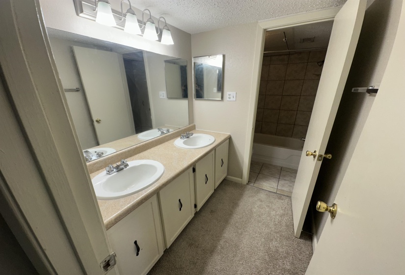 Full bathroom with a textured ceiling, double vanity, washtub / shower combination, light colored carpet, and light tile patterned floors