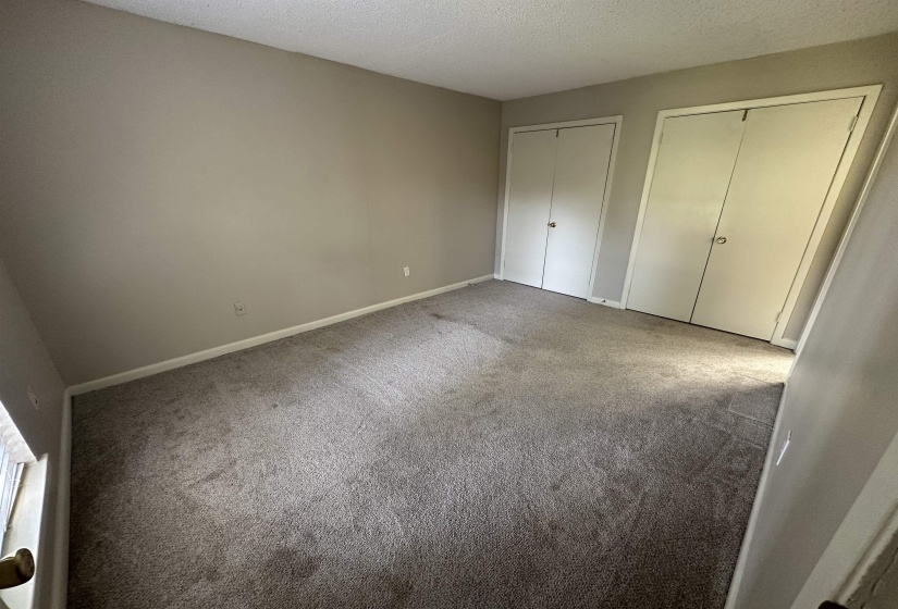 Unfurnished bedroom with a textured ceiling, two closets, and carpet flooring