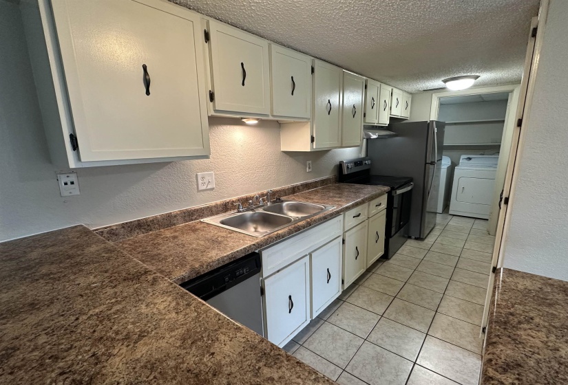 Kitchen featuring a textured wall, dark countertops, a textured ceiling, range with electric cooktop, and light tile patterned floors