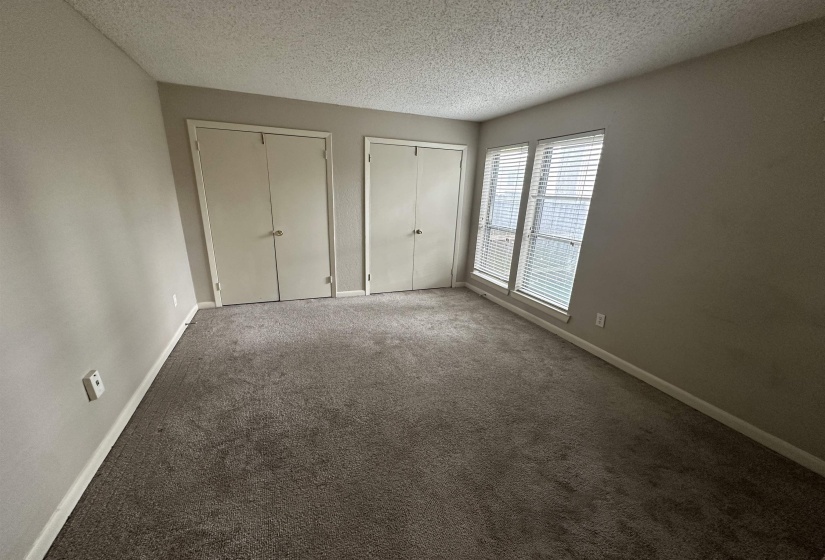 Unfurnished bedroom featuring two closets, carpet flooring, and a textured ceiling