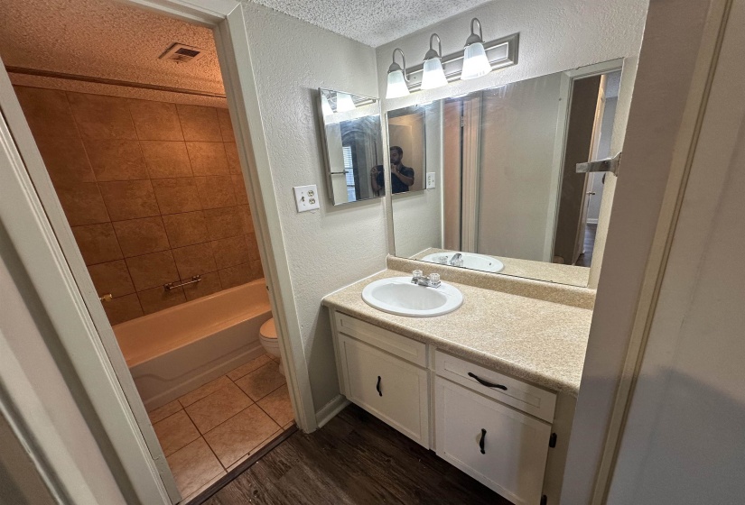 Full bath featuring a textured wall, a textured ceiling, vanity, dark wood-type flooring, and bathtub / shower combination
