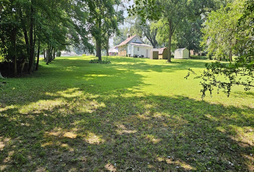 View of green lawn with a shed and view of wooded area