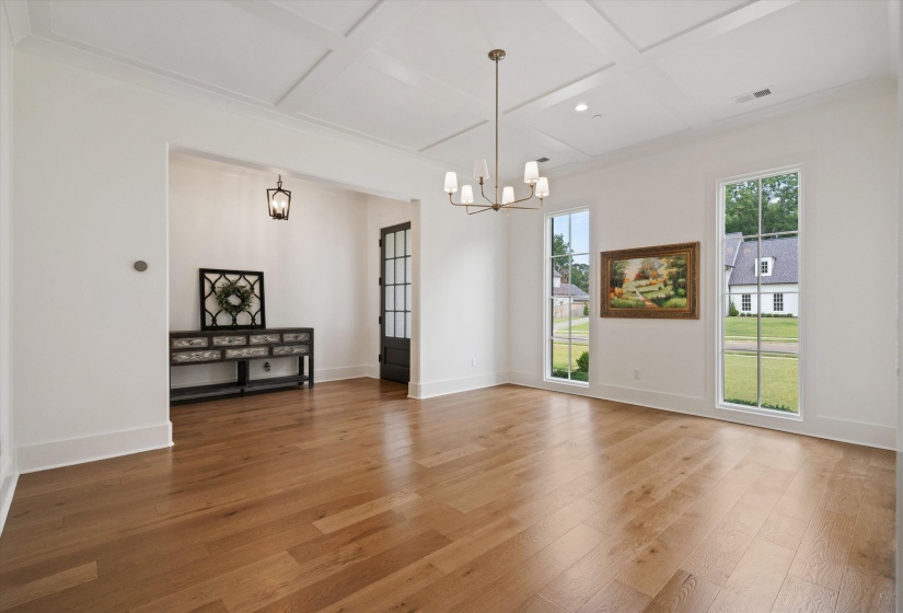Formal dining area with light wood-type flooring, coffered ceiling, and a chandelier