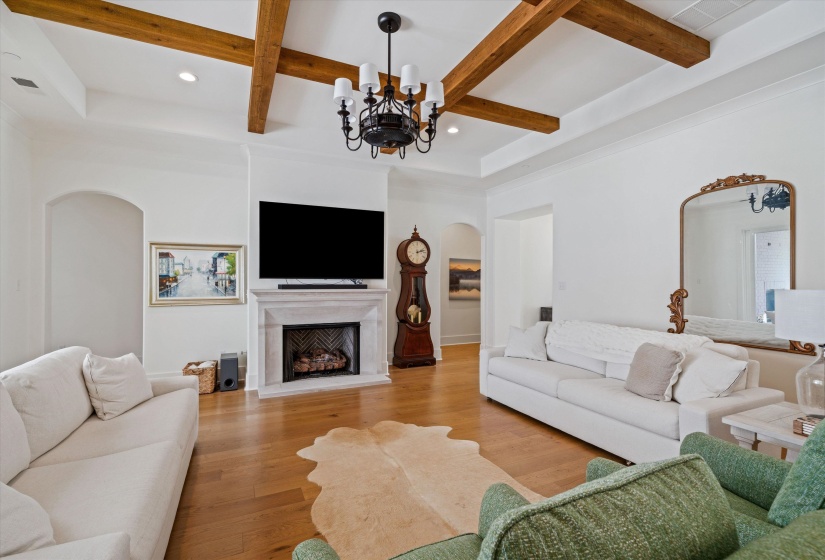 Living area featuring arched walkways, beamed ceiling, wood finished floors, a gas fireplace with raised hearth, and coffered ceiling