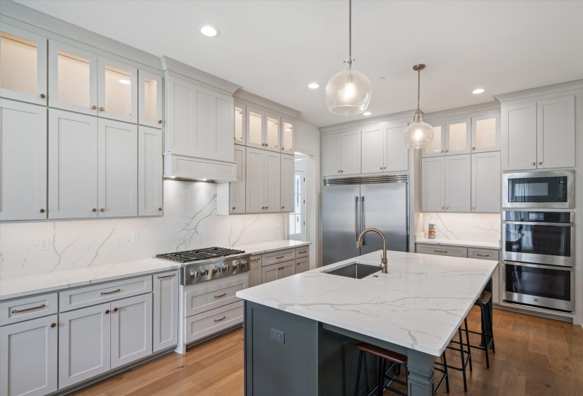 Kitchen with glass insert cabinets, a breakfast bar area, light stone counters, a center island with sink, and recessed lighting