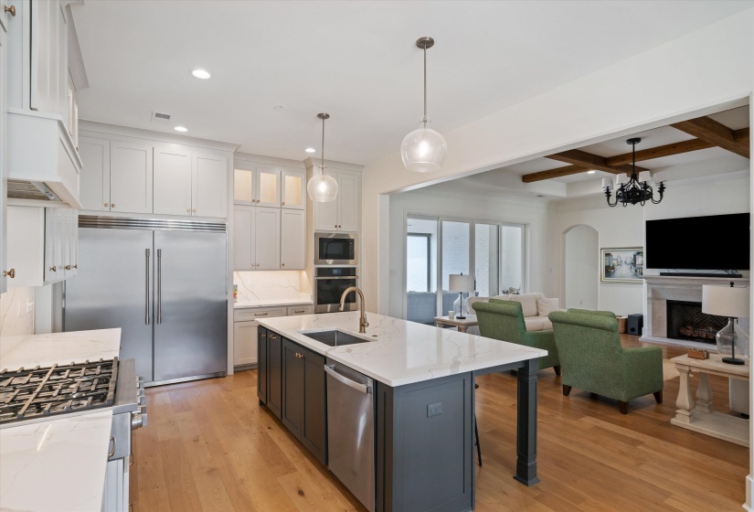 Kitchen with decorative light fixtures, light wood-style flooring, beamed ceiling, light stone countertops, and built in appliances