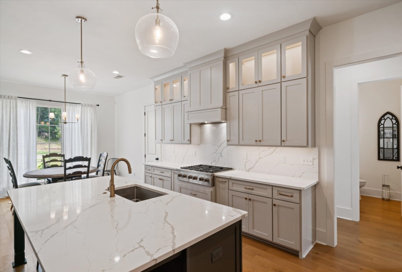 Kitchen featuring hanging light fixtures, glass insert cabinets, light stone counters, and recessed lighting