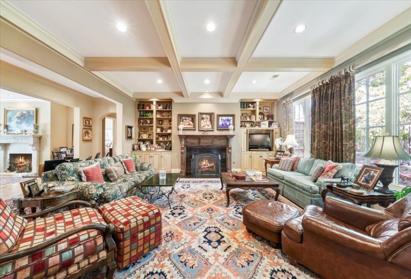 Living area with a warm lit fireplace, beamed ceiling, built in features, crown molding, and coffered ceiling