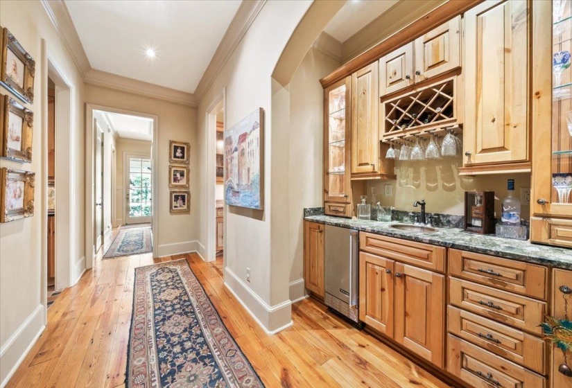 Indoor wet bar with dark stone counters, crown molding, light wood-style flooring, luxury fridge, and arched walkways