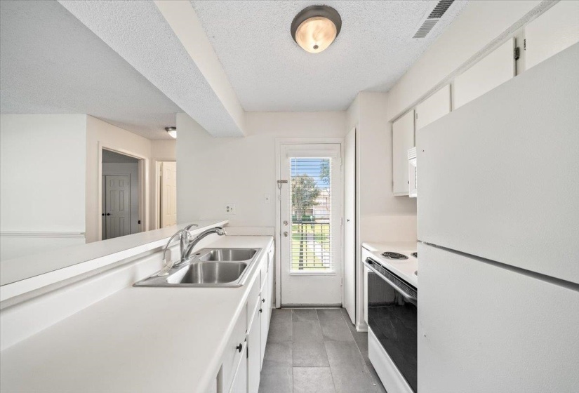 Kitchen featuring white appliances, white cabinets, light countertops, a textured ceiling, and a peninsula