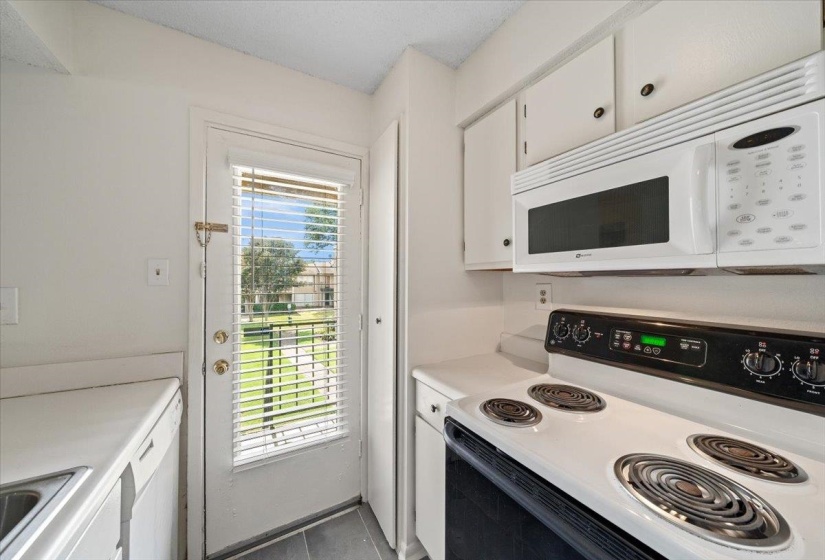 Kitchen with white appliances, white cabinets, light countertops, and dark tile patterned flooring