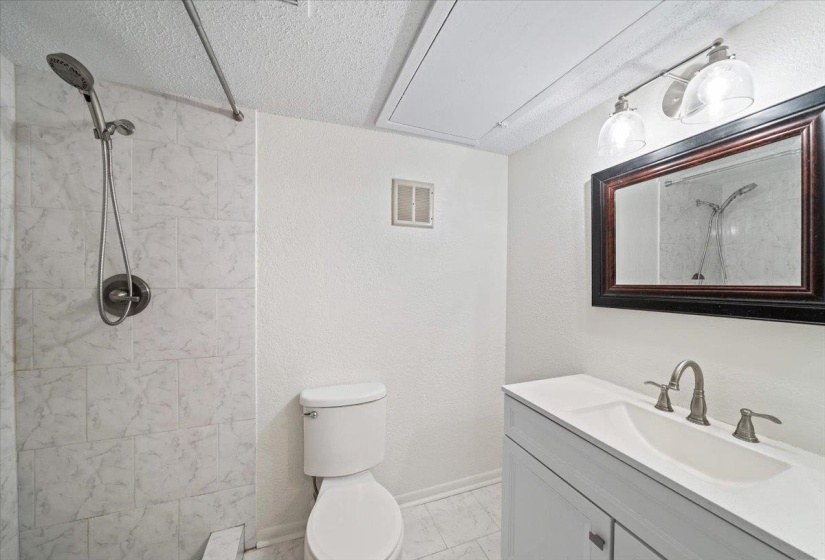 Full bathroom with vanity, a tile shower, a textured ceiling, and a textured wall