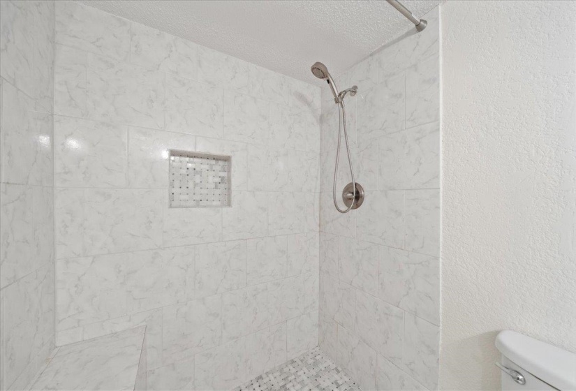Bathroom featuring a stall shower, a textured wall, and a textured ceiling