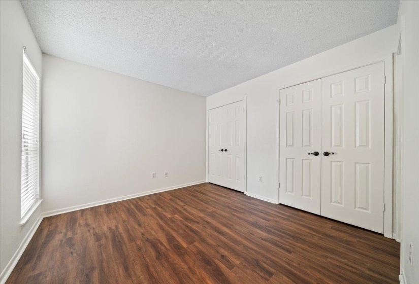 Unfurnished bedroom featuring two closets, a textured ceiling, and dark wood finished floors