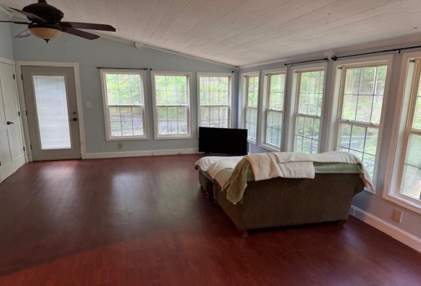 Bright living space featuring extensive window banks, wood-finish flooring, a ceiling fan, and a light-colored wood-paneled vaulted ceiling