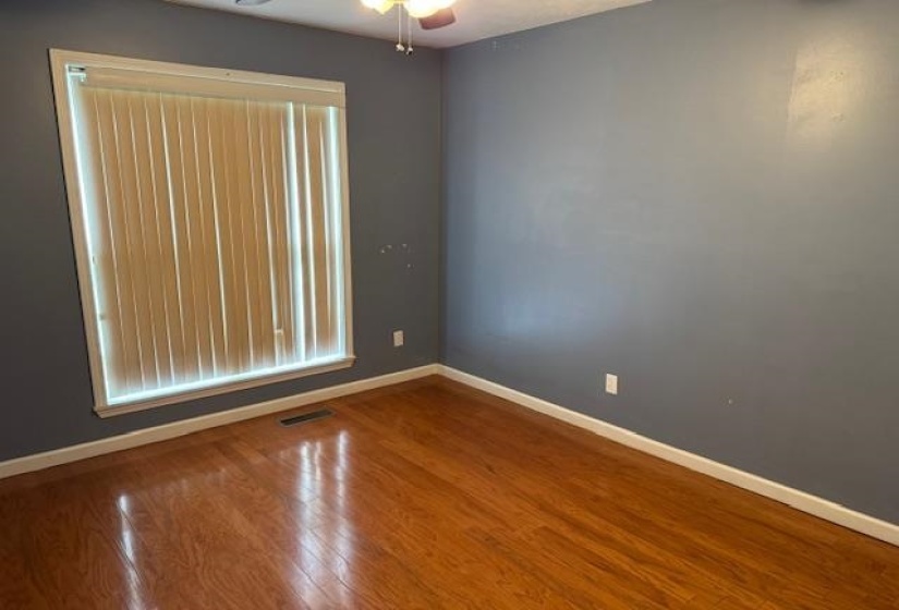 Room featuring wood-finish flooring, a window with vertical blinds, a ceiling fan with integrated lighting, and painted walls with white trim