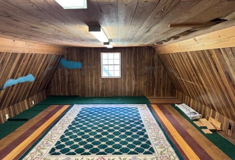 Attic space featuring wood-paneled walls and ceiling, a single window, and fluorescent lighting fixtures