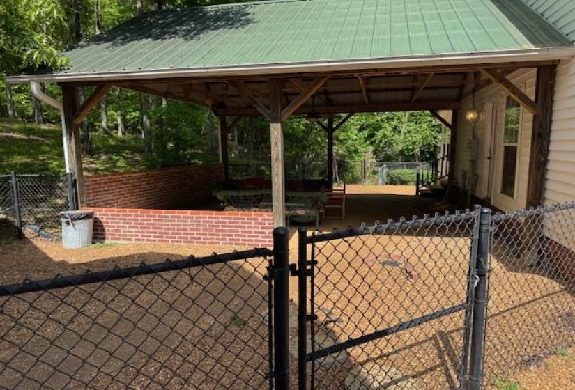 Covered outdoor patio area featuring a green metal roof, exposed wood beam framing, and a brick half-wall