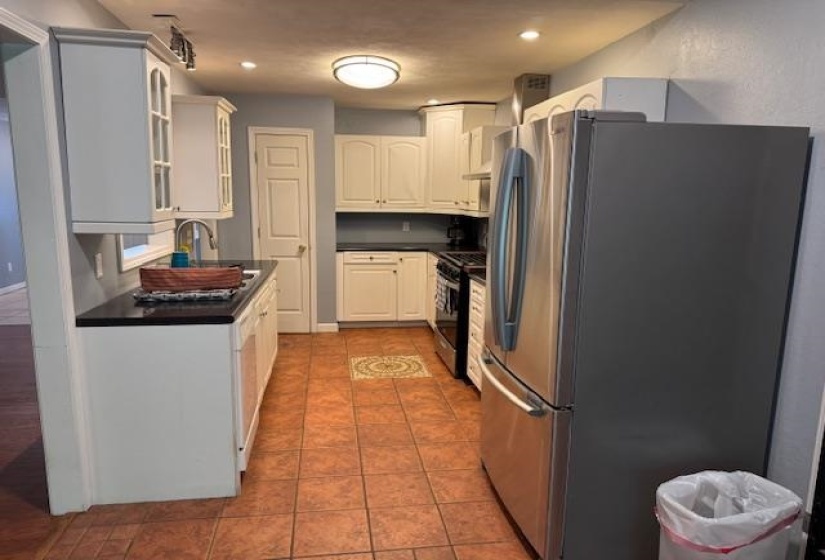 Galley-style kitchen featuring white cabinetry, dark countertops, a stainless steel refrigerator, and terracotta-toned tile flooring