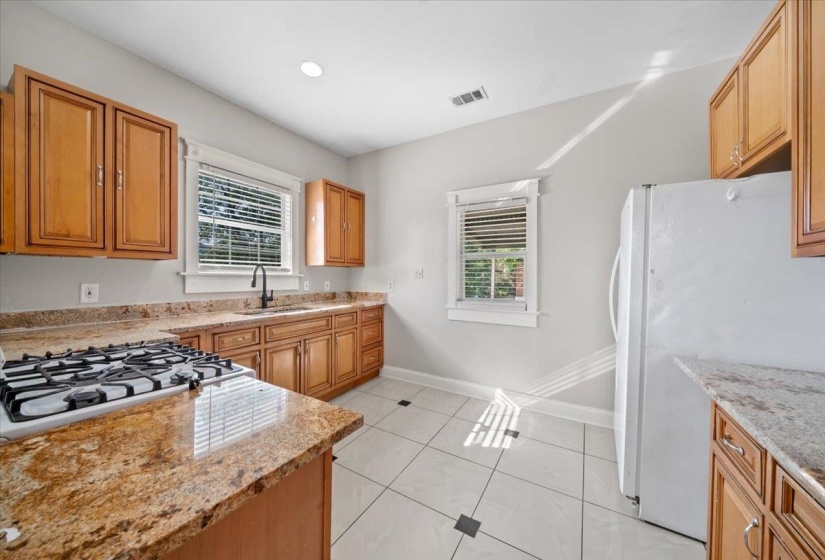 Kitchen featuring white appliances, light stone counters, light tile patterned flooring, brown cabinets, and recessed lighting