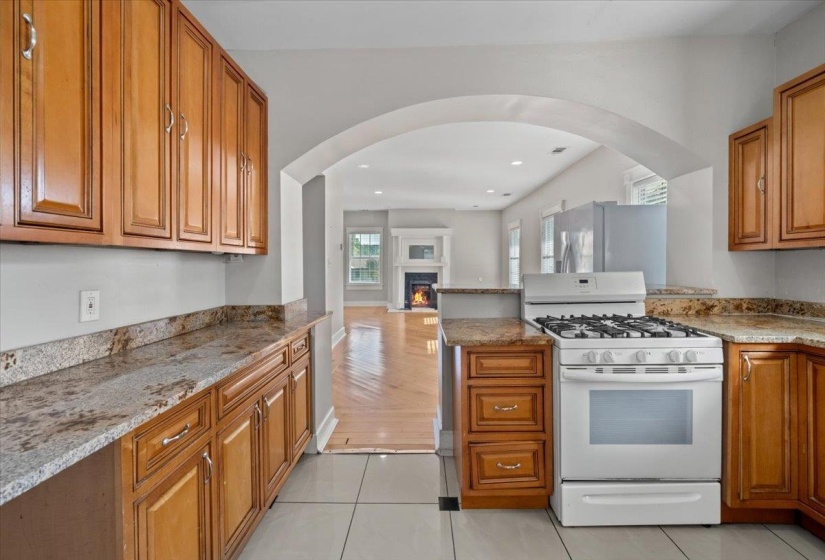Kitchen with white gas range, brown cabinetry, light stone countertops, light tile patterned floors, and recessed lighting