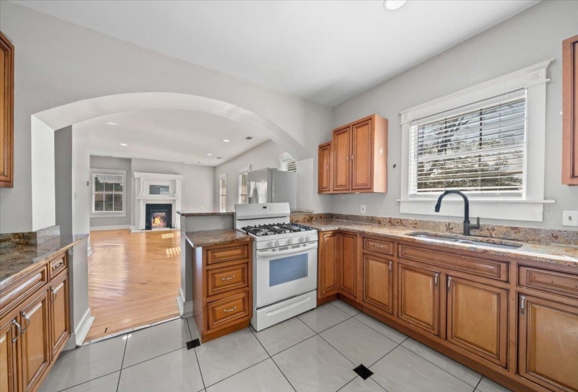 Kitchen with brown cabinets, white gas stove, a warm lit fireplace, open floor plan, and dark stone countertops