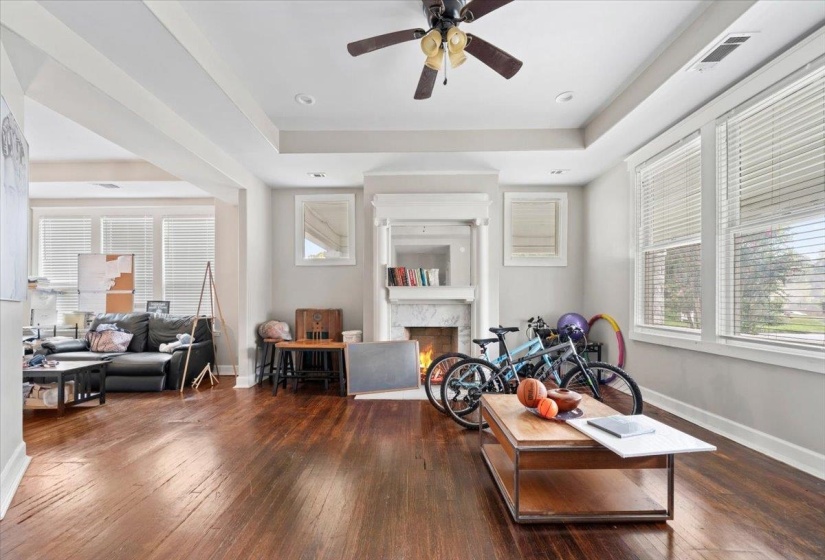 Living room featuring a tray ceiling, dark wood-type flooring, a premium fireplace, and ceiling fan