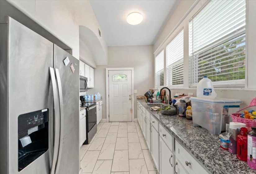 Kitchen with stainless steel appliances, white cabinetry, dark stone counters, and light marble finish flooring