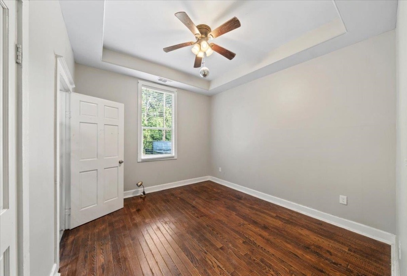Unfurnished bedroom featuring a tray ceiling, dark wood-style flooring, and ceiling fan
