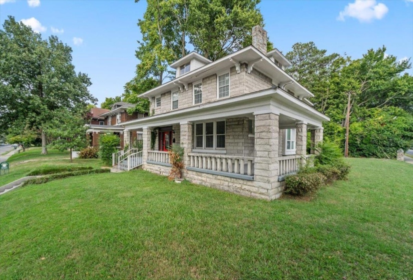 View of front of property with covered porch, a front lawn, a chimney, and stone siding
