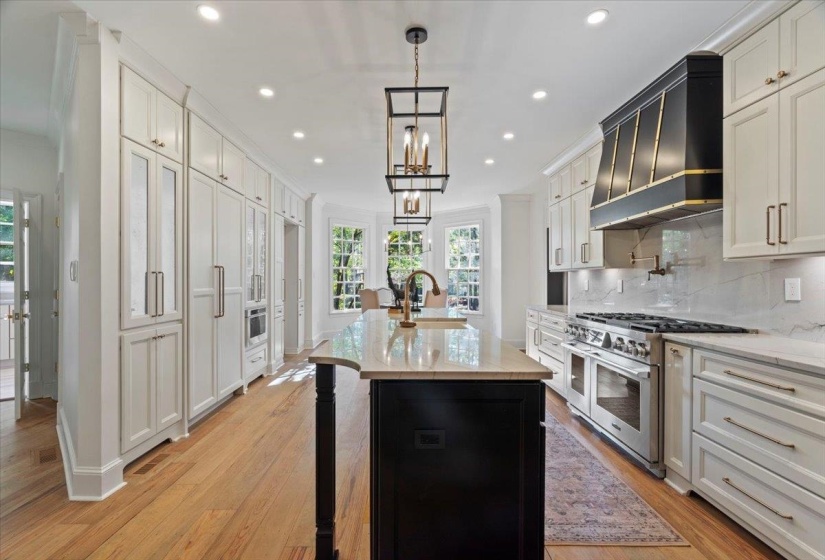 Kitchen with light stone counters, custom range hood, range with two ovens, decorative light fixtures, and decorative backsplash