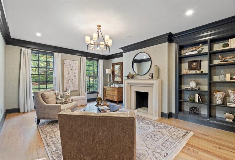 Living area with crown molding, a fireplace with flush hearth, light wood-style floors, a chandelier, and built in features
