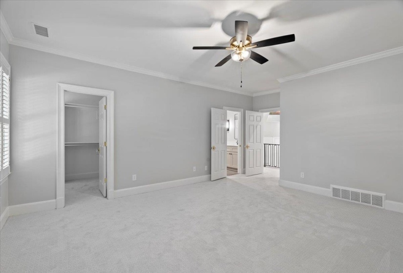 Unfurnished bedroom with ornamental molding, a walk in closet, light colored carpet, and ceiling fan
