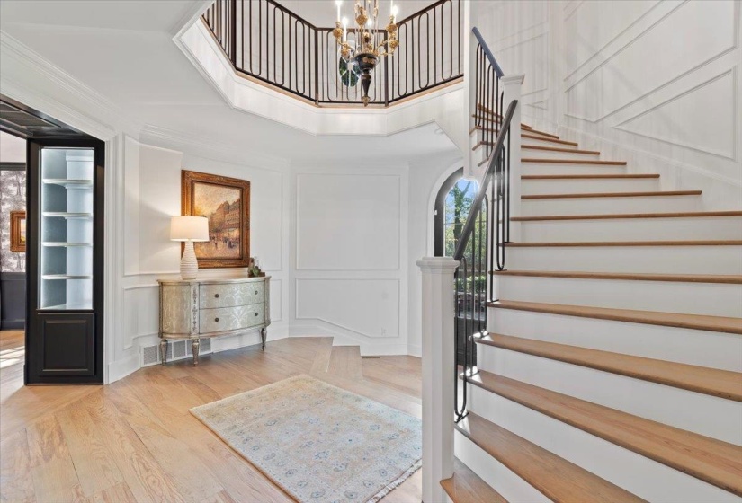 Foyer entrance with a decorative wall, light wood-style floors, a high ceiling, a chandelier, and arched walkways