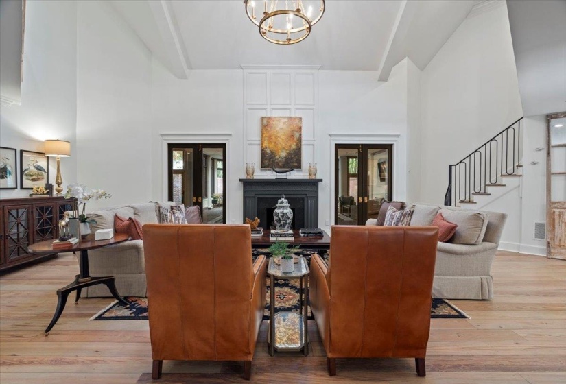 Living room featuring a towering ceiling, light wood-type flooring, a fireplace, a chandelier, and stairway