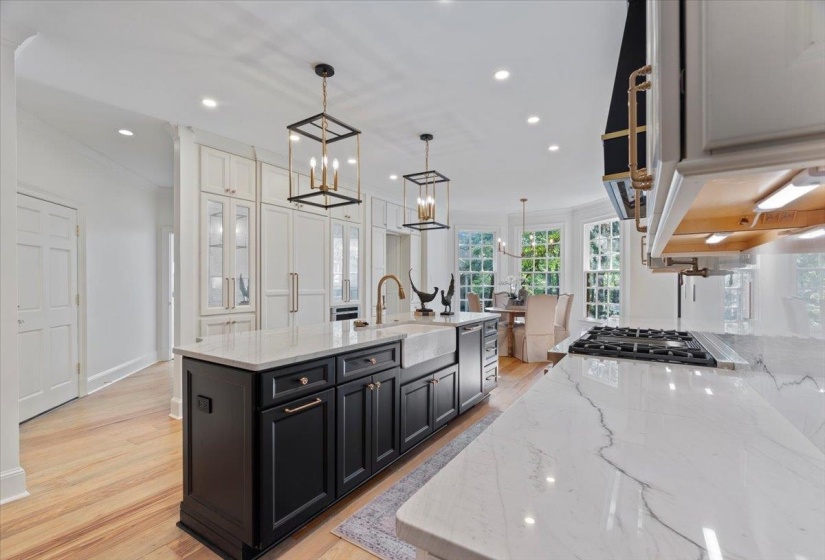 Kitchen featuring dark cabinetry, light stone countertops, light wood-type flooring, recessed lighting, and crown molding