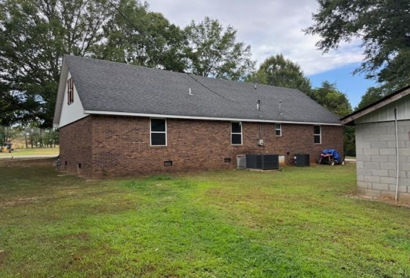 Back of property with crawl space, a lawn, brick siding, and a shingled roof