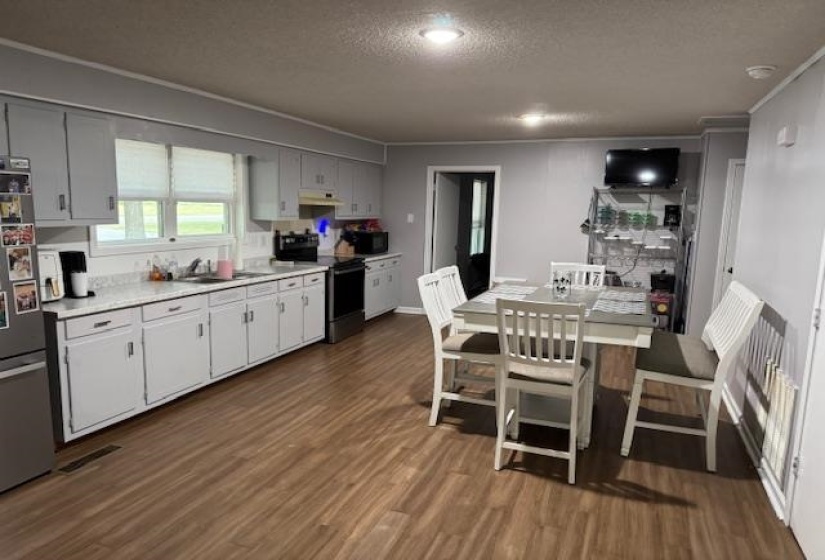 Kitchen with a textured ceiling, light countertops, appliances with stainless steel finishes, dark wood-type flooring, and ornamental molding