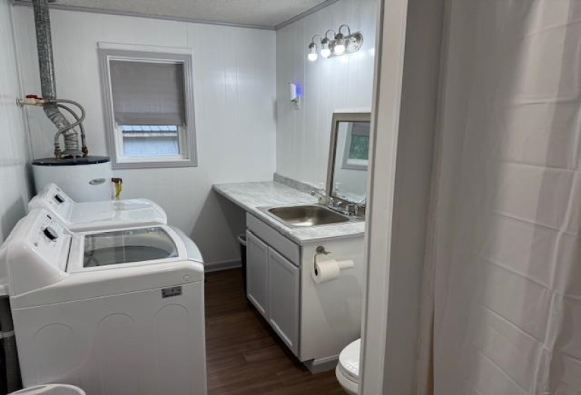 Bathroom featuring dark wood finished floors, vanity, washer and clothes dryer, and water heater