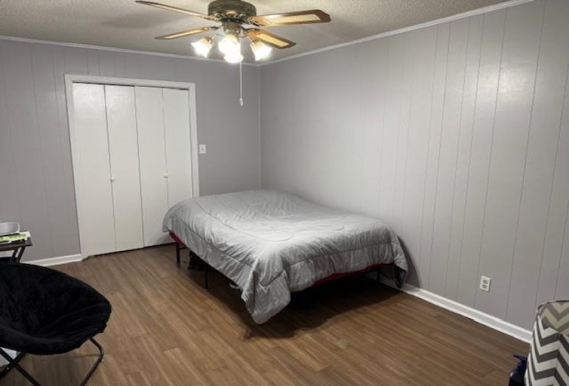 Bedroom with dark wood-style flooring, crown molding, a textured ceiling, wooden walls, and ceiling fan