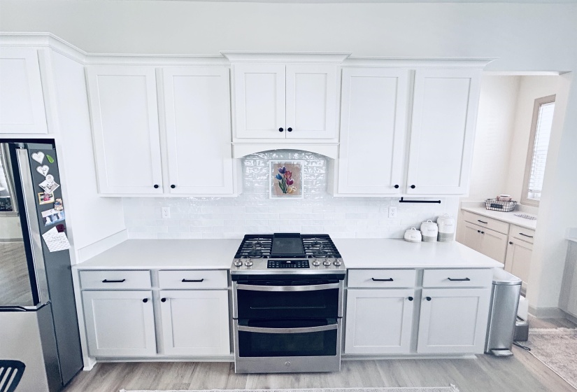 Kitchen with stainless steel appliances, white cabinets, decorative backsplash, and light wood-style flooring