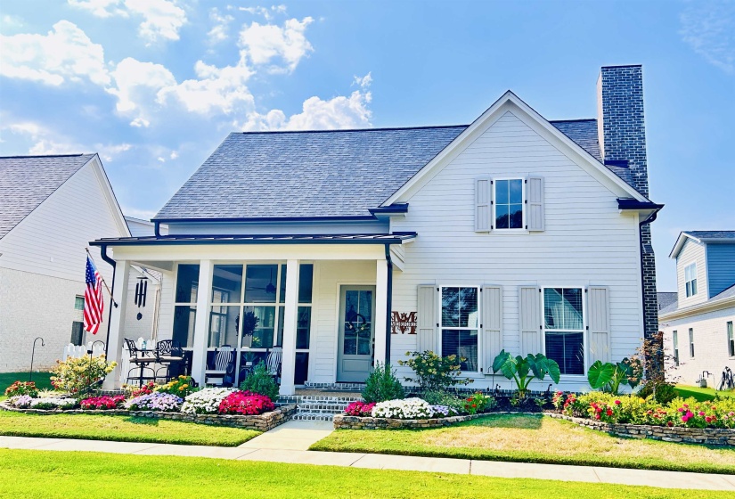 View of front of home with covered porch, a chimney, a front lawn, and a shingled roof