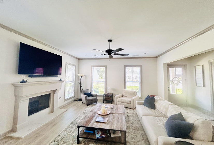 Living area featuring wood finished floors, crown molding, ceiling fan, and a fireplace with raised hearth